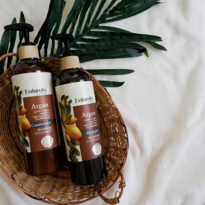 Flat lay of argan oil shampoo and conditioner in a basket with green leaves, perfect for haircare routines.