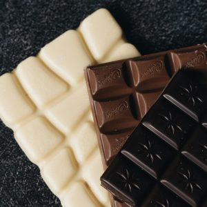 Close-up of assorted white, milk, and dark chocolate bars on a textured surface.