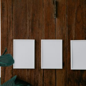 Three blank white frames on rustic wooden wall with green leaves for a clean, minimalist design.